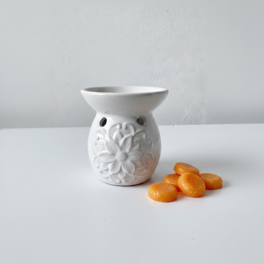 Quemador de cerámica blanca con wax melts de mandarina sobre fondo blanco